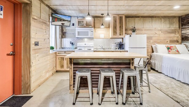Eine kompakte Küche mit Holzausstattung, einer zentralen Kochinsel mit Barhocker, einer Mikrowelle und einem Kühlschrank.