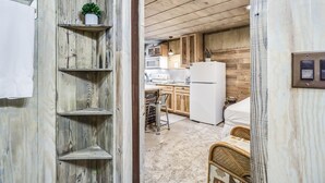 Ein schmaler Flur mit Holzregalen, einem weißen Kühlschrank und einem Bett im Hintergrund.