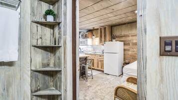 A narrow hallway with wooden shelves, a white refrigerator, and a bed in the background.