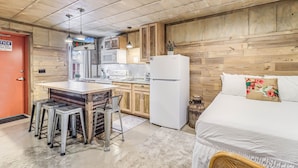 Eine kompakte Küche mit Holzschränken, einem Kühlschrank und einer Essecke mit Hockern.