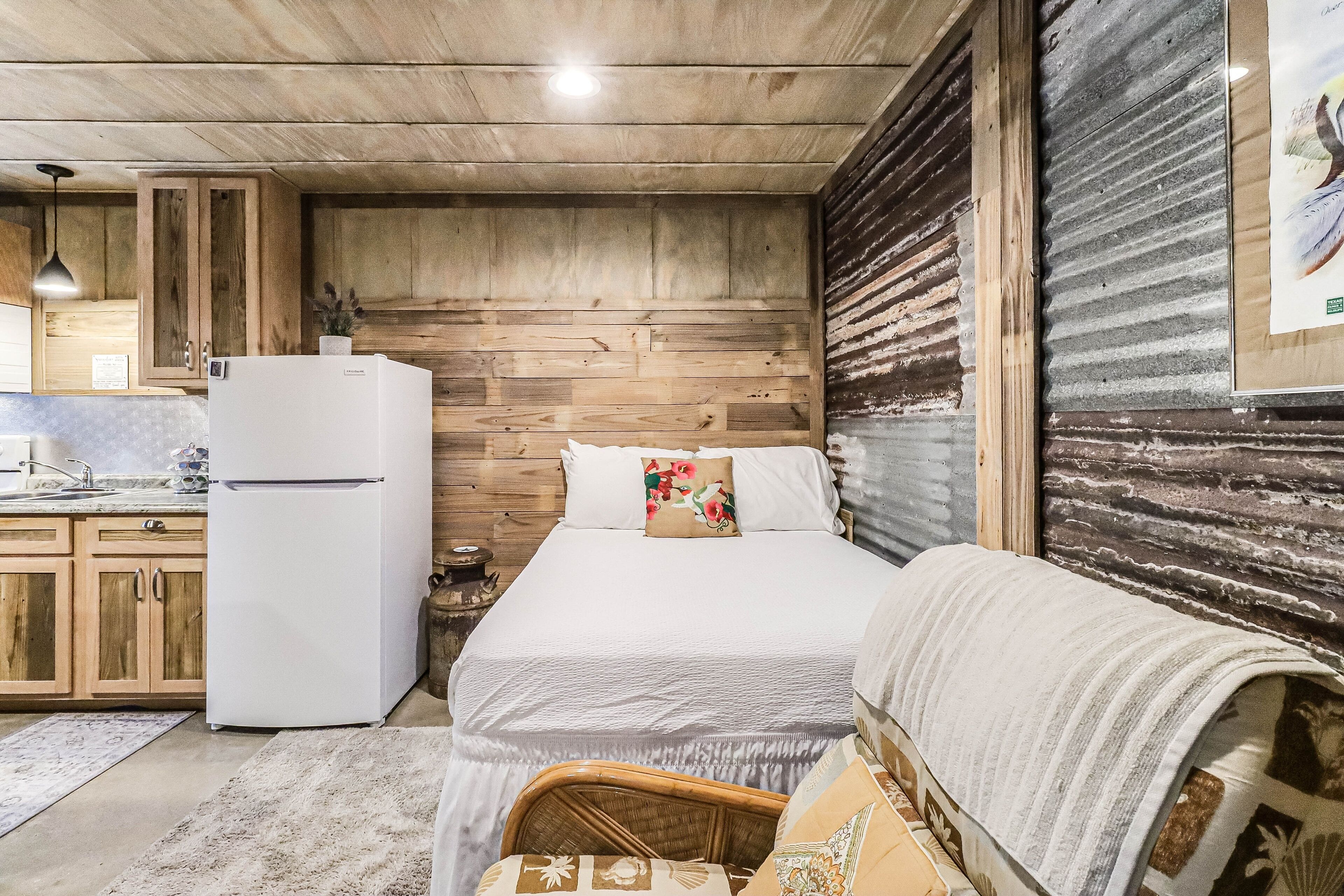 Habitación compacta con cama, kitchenette pequeña y techo de madera.