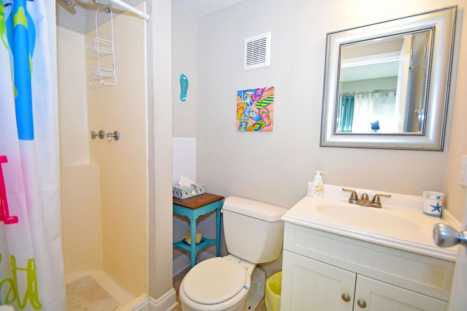 A bathroom with a shower, toilet, sink, and a mirror.