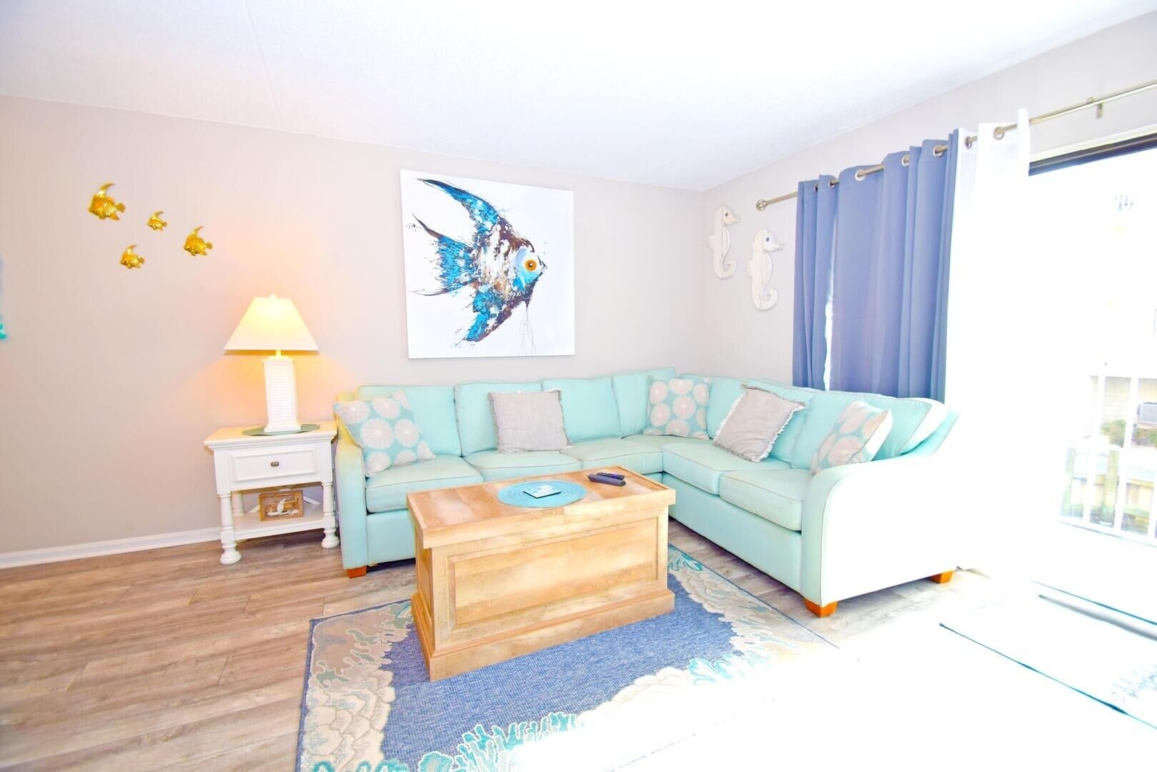 A living room with a light blue sofa, a wooden coffee table, a side table with a lamp, and a large abstract painting on the wall.