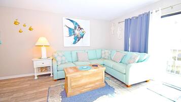 A living room with a light blue sofa, a wooden coffee table, a side table with a lamp, and a large abstract painting on the wall.