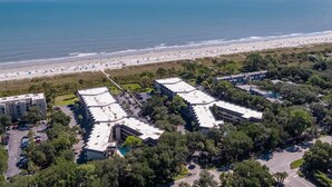Vista aérea de un hotel costero con varias edificaciones, un estacionamiento y una playa al fondo.