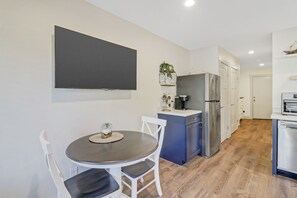 A modern kitchen with a dining area, featuring a refrigerator, oven, and a flat-screen TV mounted on the wall. - Newly Renovated Villa! (Hilton Head Island)