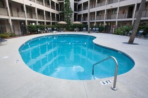 A pool with a 3 FT depth marker, surrounded by lounge chairs and umbrellas, with a multi-story building in the background. - Newly Renovated Villa! (Hilton Head Island)