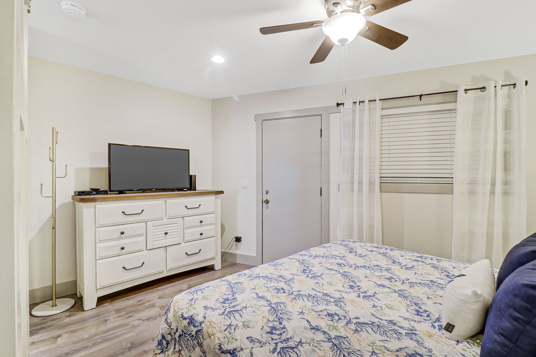 A bedroom with a bed, a TV on a dresser, a ceiling fan, and a door.