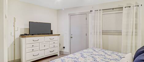 A bedroom with a bed, a TV on a dresser, a ceiling fan, and a door.