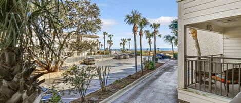 A street with palm trees, a parking lot, and a building with a balcony.