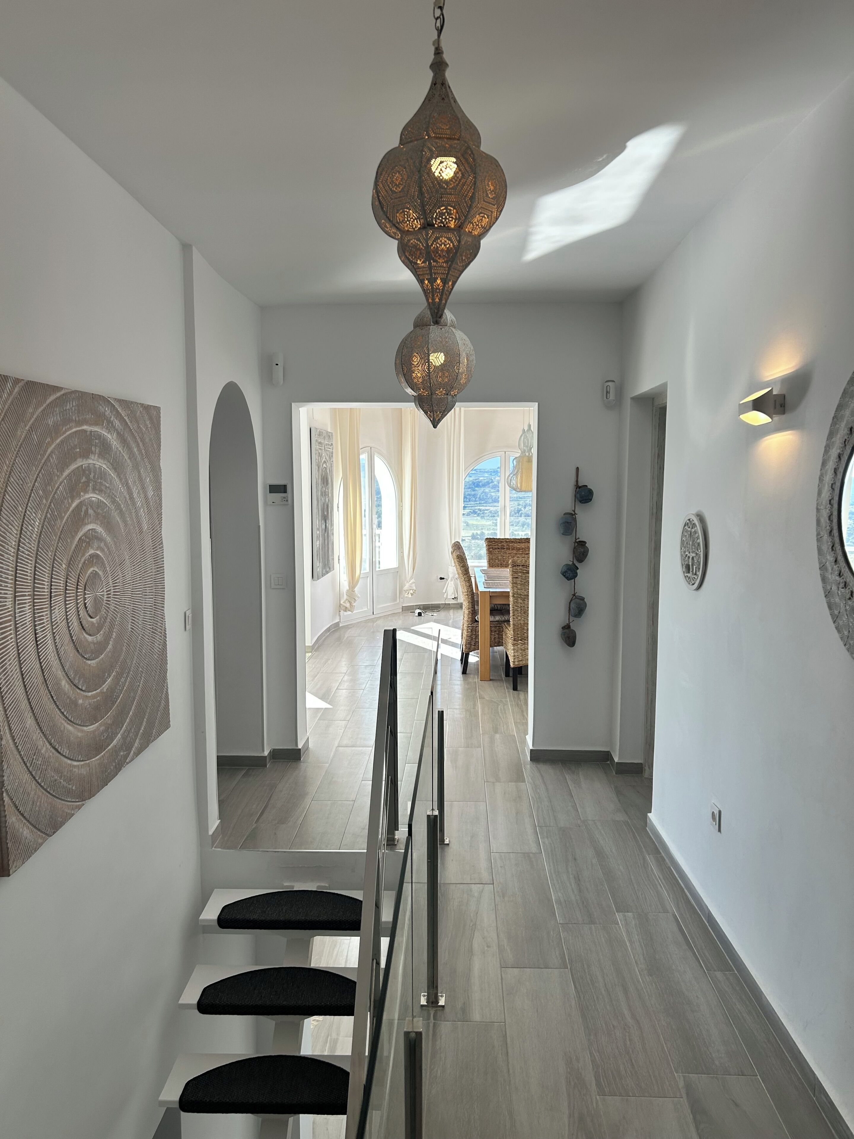 Ein modernes Interieur mit Treppe, einer Hängelampe und Blick durch eine offene Tür.