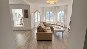 Ein geräumiges Wohnzimmer mit Ecksofa, Couchtisch und großen Fenstern mit Blick ins Freie.