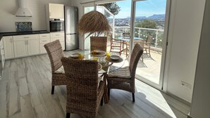 Eine moderne Küche mit weißen Schränken, ein Essbereich mit Korbstühlen und eine große Schiebeglastür, die auf einen Balkon mit Stadtblick führt.