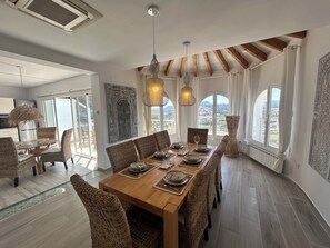 A dining area with a long wooden table, wicker chairs, and pendant lights.
