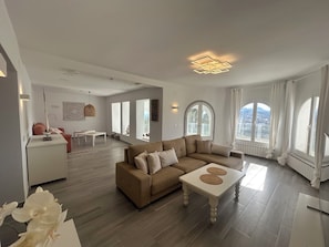 A spacious living area with a sofa, coffee table, and a view of a cityscape through large windows.