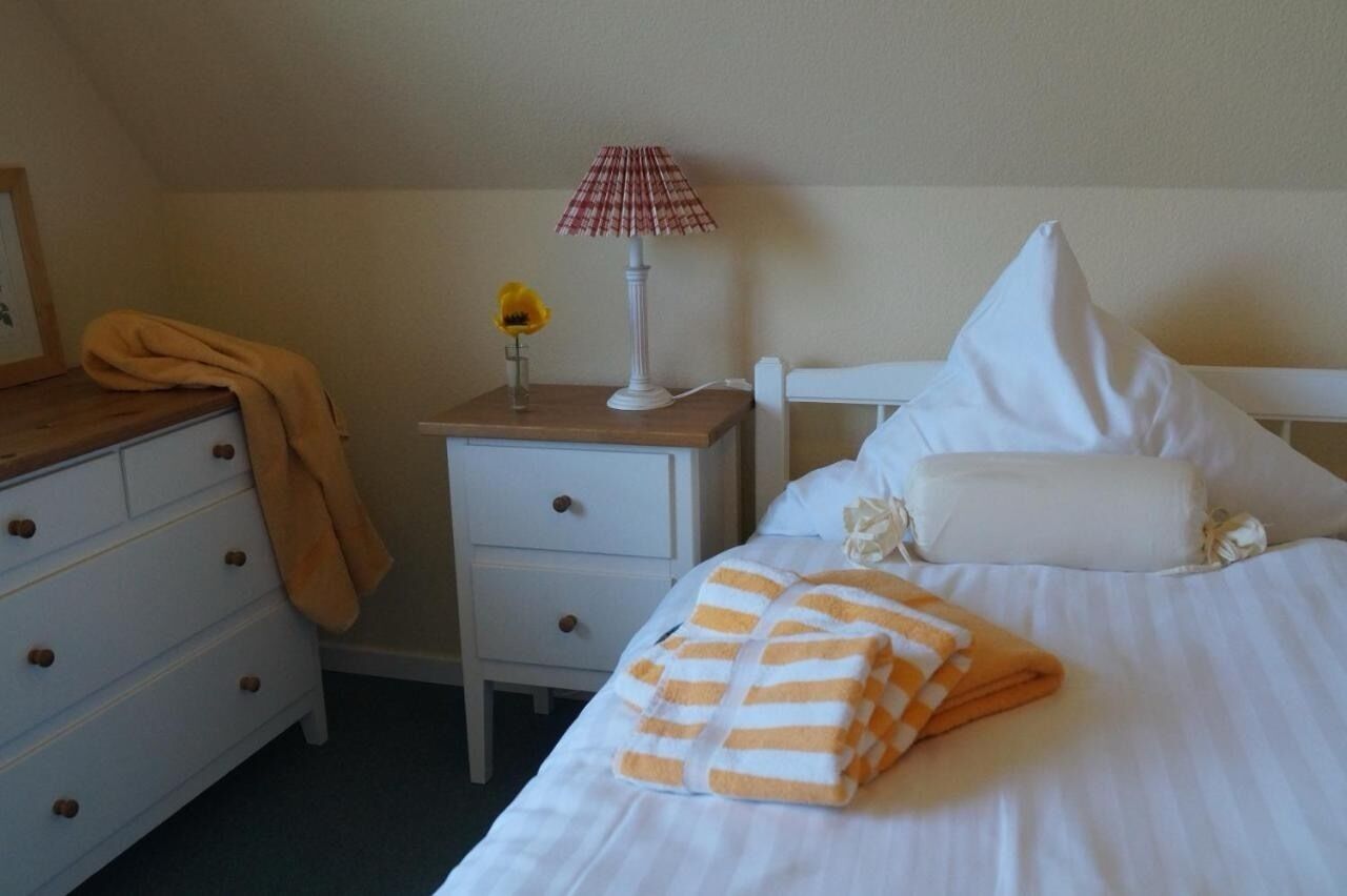 A neatly made bed with a striped blanket, a white pillow, and a small bedside table with a lamp and a vase with a single flower.