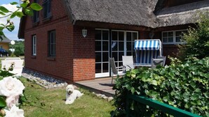 A brick house with a thatched roof, a patio with outdoor furniture, and a dog in the yard.