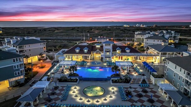 A resort with a swimming pool, lounge areas, and a view of the ocean at dusk.