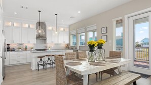 A modern kitchen with white cabinets, a large island, and a dining area with wicker chairs and a wooden bench.