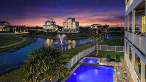 A waterfront property with a swimming pool, a fountain, and a view of the sunset over the ocean.