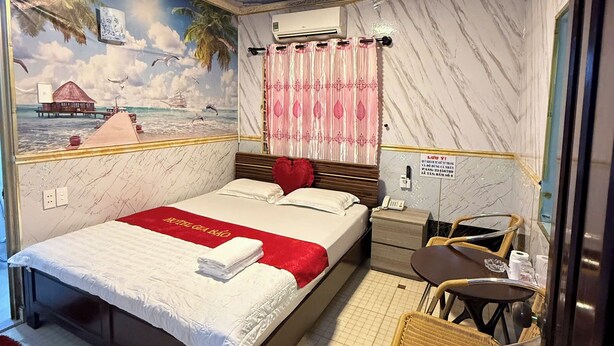 A hotel room with a bed, a small table, a chair, a ceiling fan, and a mural of a tropical scene. - Gia Bao Hotel Binh Thanh - by BayLuxury (Ho Chi Minh City)