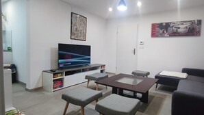 Ein Wohnzimmer mit Flachbildfernseher, grauem Sofa, Hocker und Couchtisch.