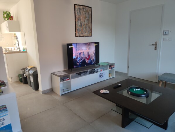 A living room with a flat-screen TV, a coffee table with playing cards, and a small pool table.