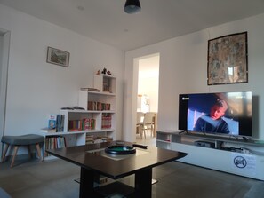 Un salon avec un téléviseur, des étagères à livres, une table basse et, au fond, un coin repas.