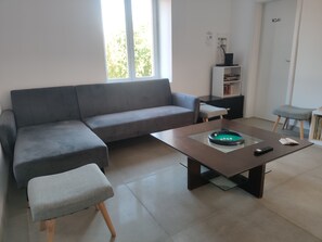 Un salon moderne avec un canapé gris, une table basse en verre et un petit pouf.