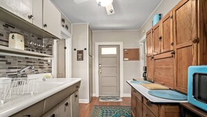Una cocina con encimera blanca, armarios de madera, microondas azul y alfombra estampada.