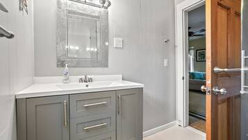 A bathroom with a white sink, grey cabinets, and a mirror with lights.