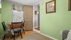 Un comedor con una mesa y sillas de madera, una ventana con persianas y una pared verde con un cuadro enmarcado.