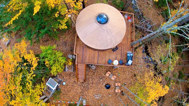 An aerial view of a wooden deck with a circular roof, surrounded by trees with yellow leaves. - A yurt in the trees.  Close to Portland but close to nature.  Treeyurt Maine (Cumberland)