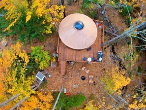 An aerial view of a wooden deck with a circular roof, surrounded by trees with yellow leaves.