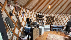 A yurt interior with a kitchen area, seating, and a hanging light fixture. - A yurt in the trees.  Close to Portland but close to nature.  Treeyurt Maine (Cumberland)