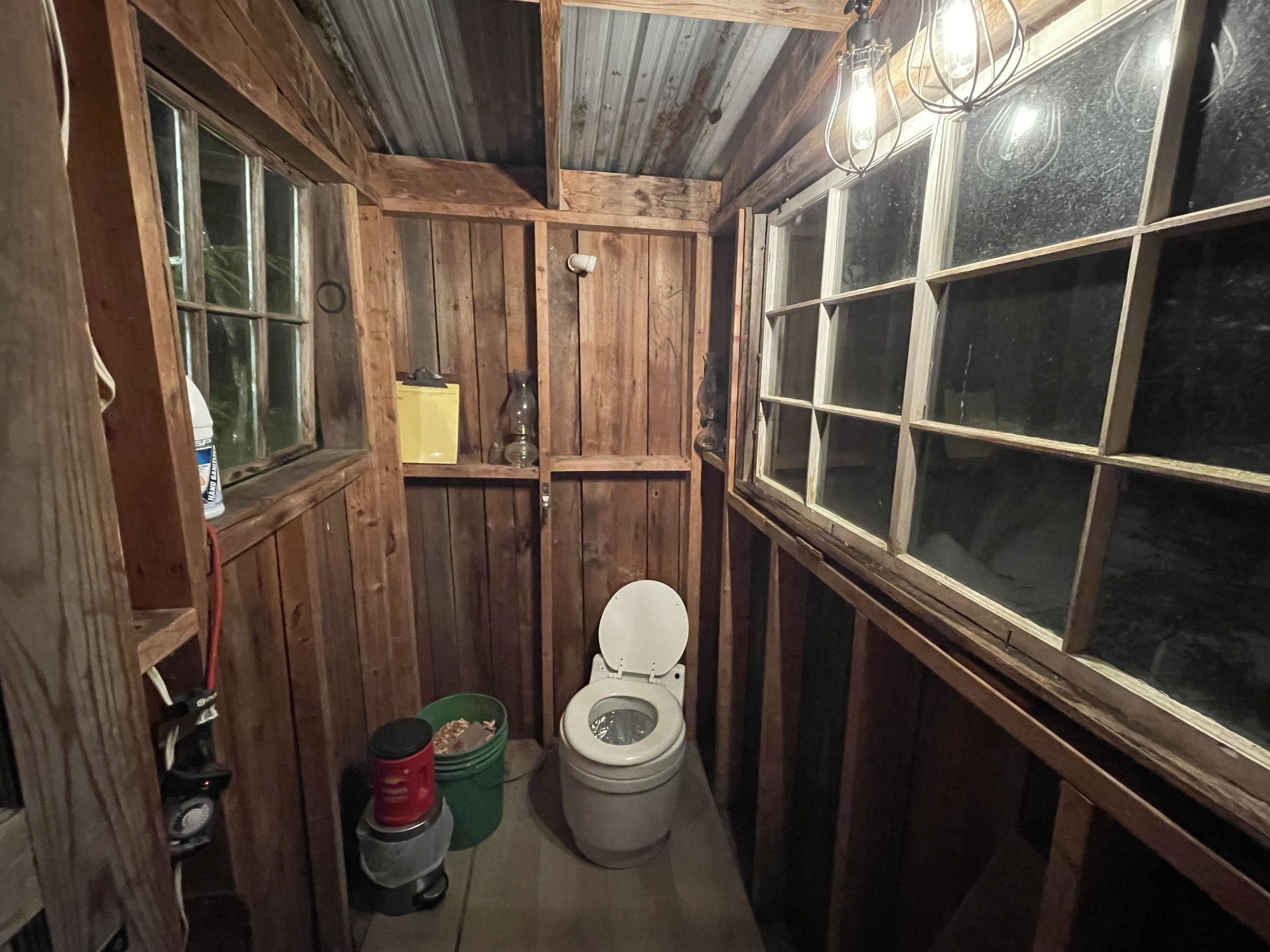 Een rustieke houten badkamer met een toilet, een plankje met een vaas en een raam.