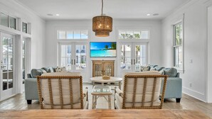 A spacious living room with two sofas facing a television, a wooden coffee table, and a wicker chair. - Seas The Moments: Next to beach walkover, across the street from the pool! (Panama City Beach)