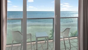 Un balcone con vista sull'oceano, con due sedie bianche e un tavolino.