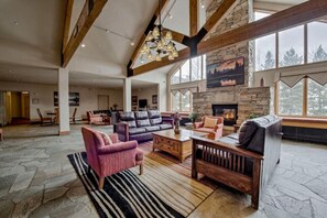 A spacious living room with a stone fireplace, large windows, and a high ceiling with exposed beams. - Walk to Keystone Lifts! Cozy Studio w/ Mountain Views, Pool & Hot Tub (Keystone)