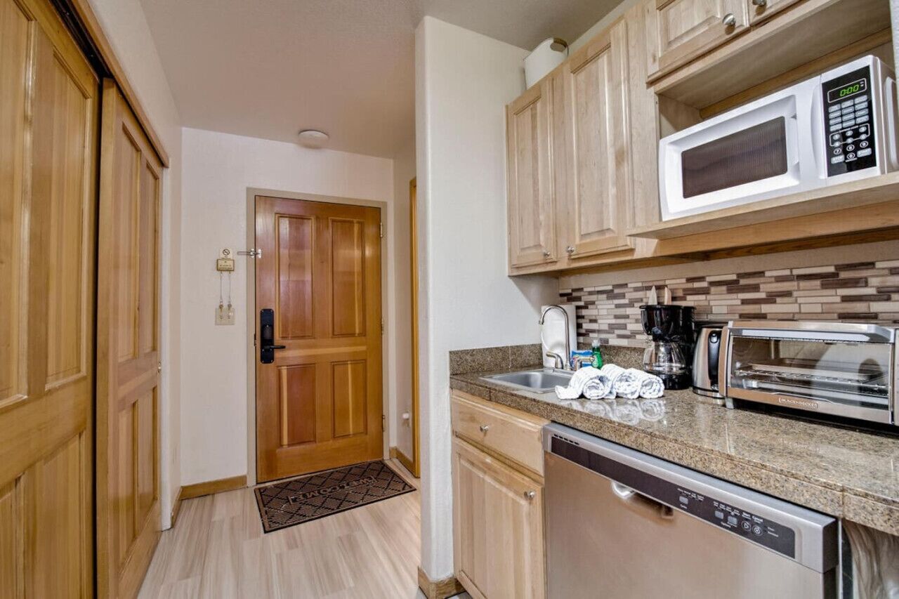 Una cocina compacta con muebles de madera, microondas, tostadora y lavavajillas.