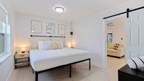 Une chambre à coucher comprenant un lit, des tables de chevet, une commode, une lampe fixée au mur et une porte donnant sur une autre pièce.