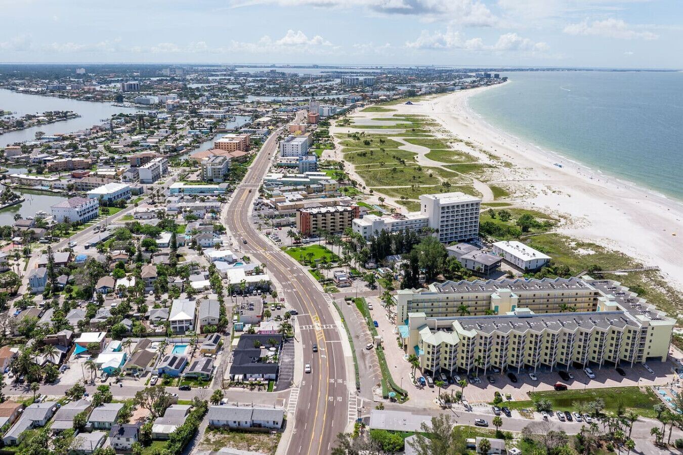 Une vue aérienne d’une ville côtière, avec une route principale bien visible, une plage et un grand hôtel à plusieurs étages, doté d’un parking.