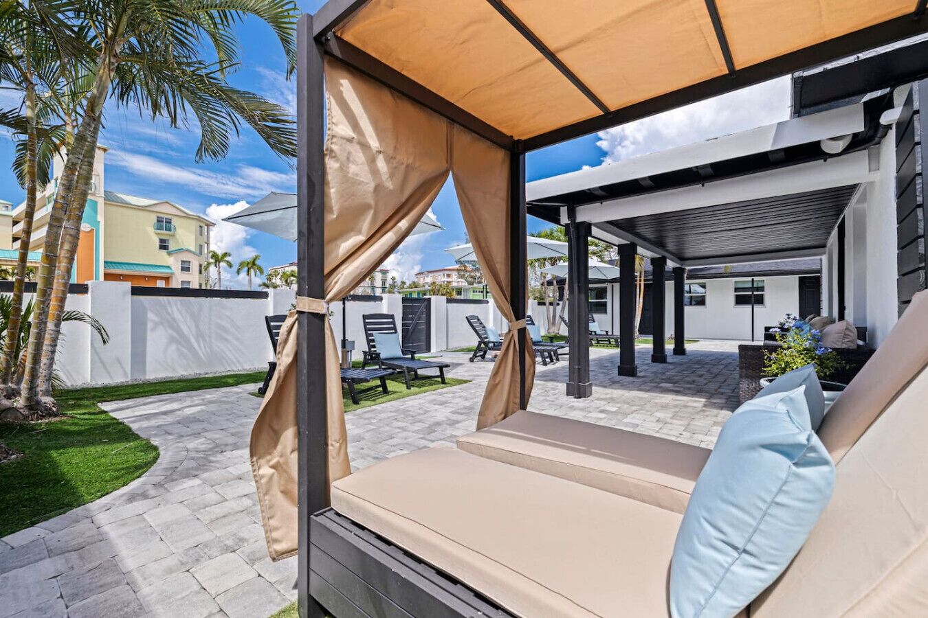 A covered outdoor seating area with a cushioned bench, a pergola structure, and a view of a residential neighborhood.