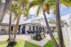 A modern outdoor patio with lounge chairs and a covered seating area, surrounded by palm trees and a building with a white exterior. - Las Olas of Treasure Island #9 (Treasure Island)