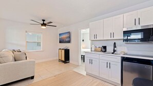 Una cocina moderna con armarios blancos, un microondas negro y un lavavajillas. Hay un sofá color beige y un mueble pequeño con adornos.