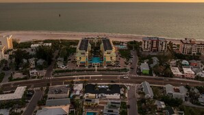 An aerial view of a coastal area with a prominent hotel featuring a central courtyard, adjacent to a beach.