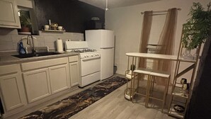 Una cocina con gabinetes blancos, estufa, refrigerador y ventilador de techo.