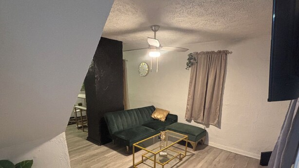 Una sala de estar con un sofá verde, una mesa de centro de vidrio y un ventilador de techo.