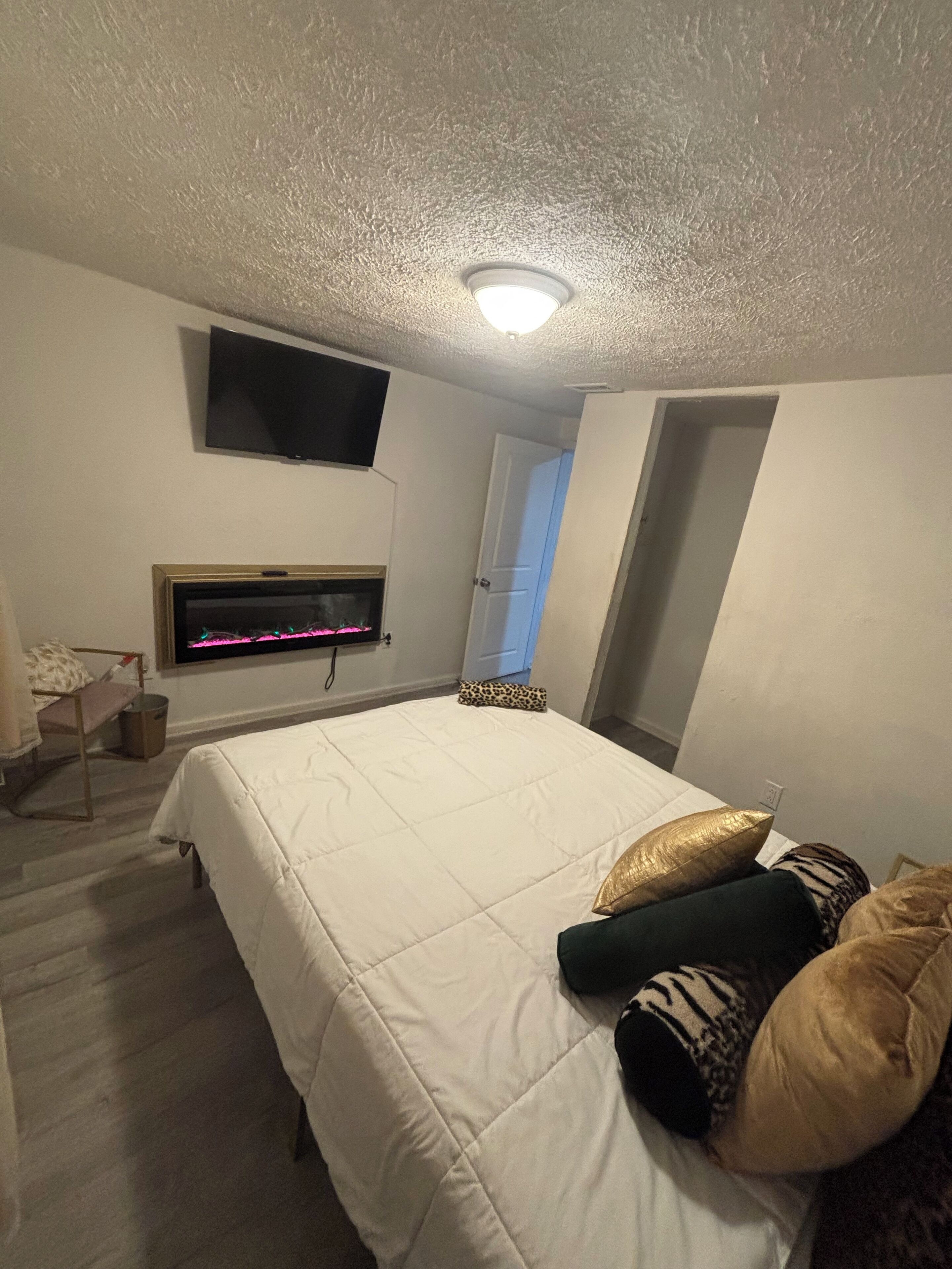A bedroom with a bed, a flat-screen TV mounted on the wall, and a fireplace.