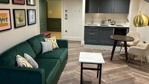 A modern living room with a green sofa, a small table, and a kitchen area with dark cabinets and a white countertop. - TheHillbrookSherborne (Sherborne)